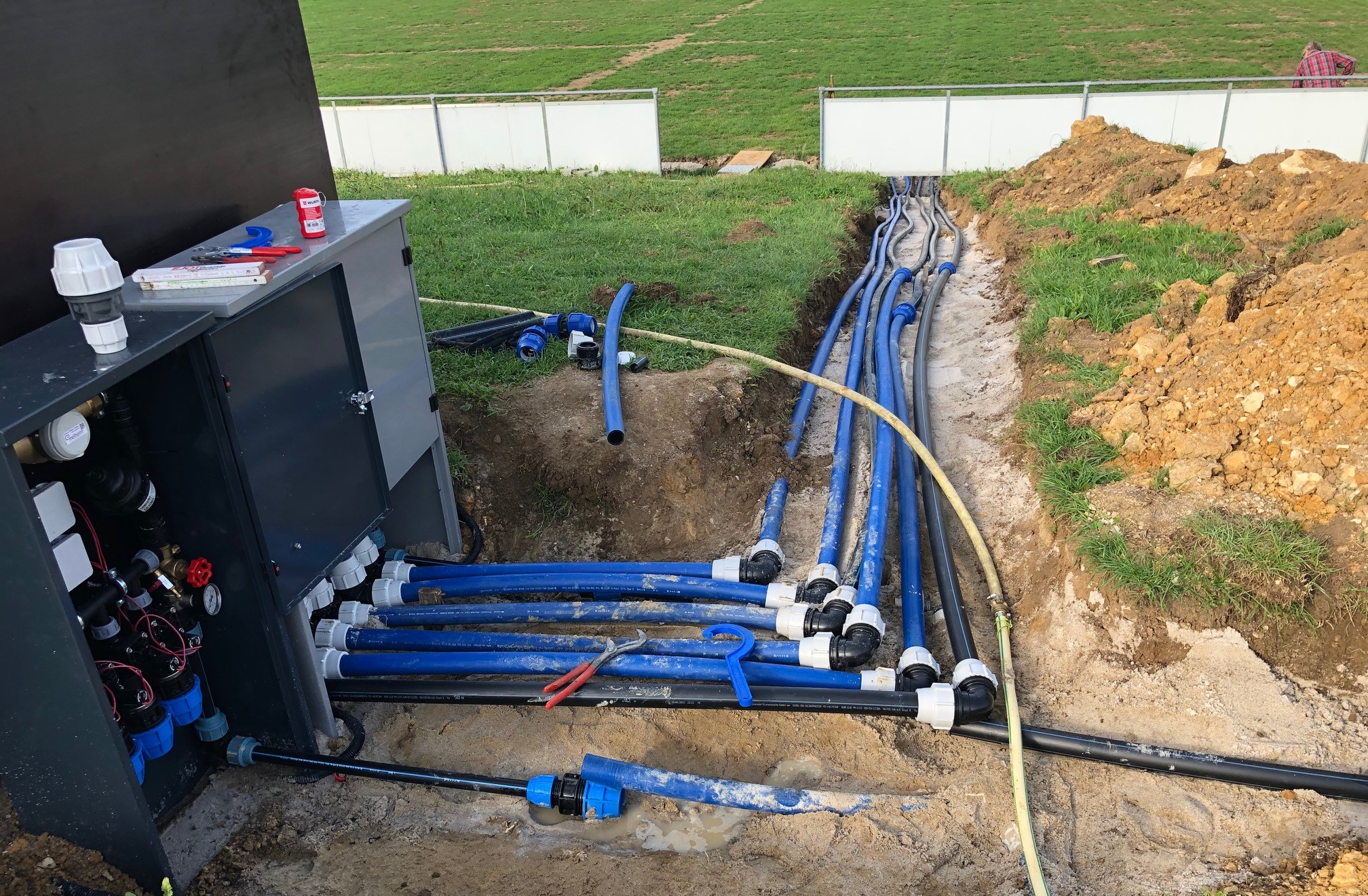 Geöffneter Verteilerschrank der IRRIGATECS® Anlage während der Installation, angeschlossene Stränge im Graben